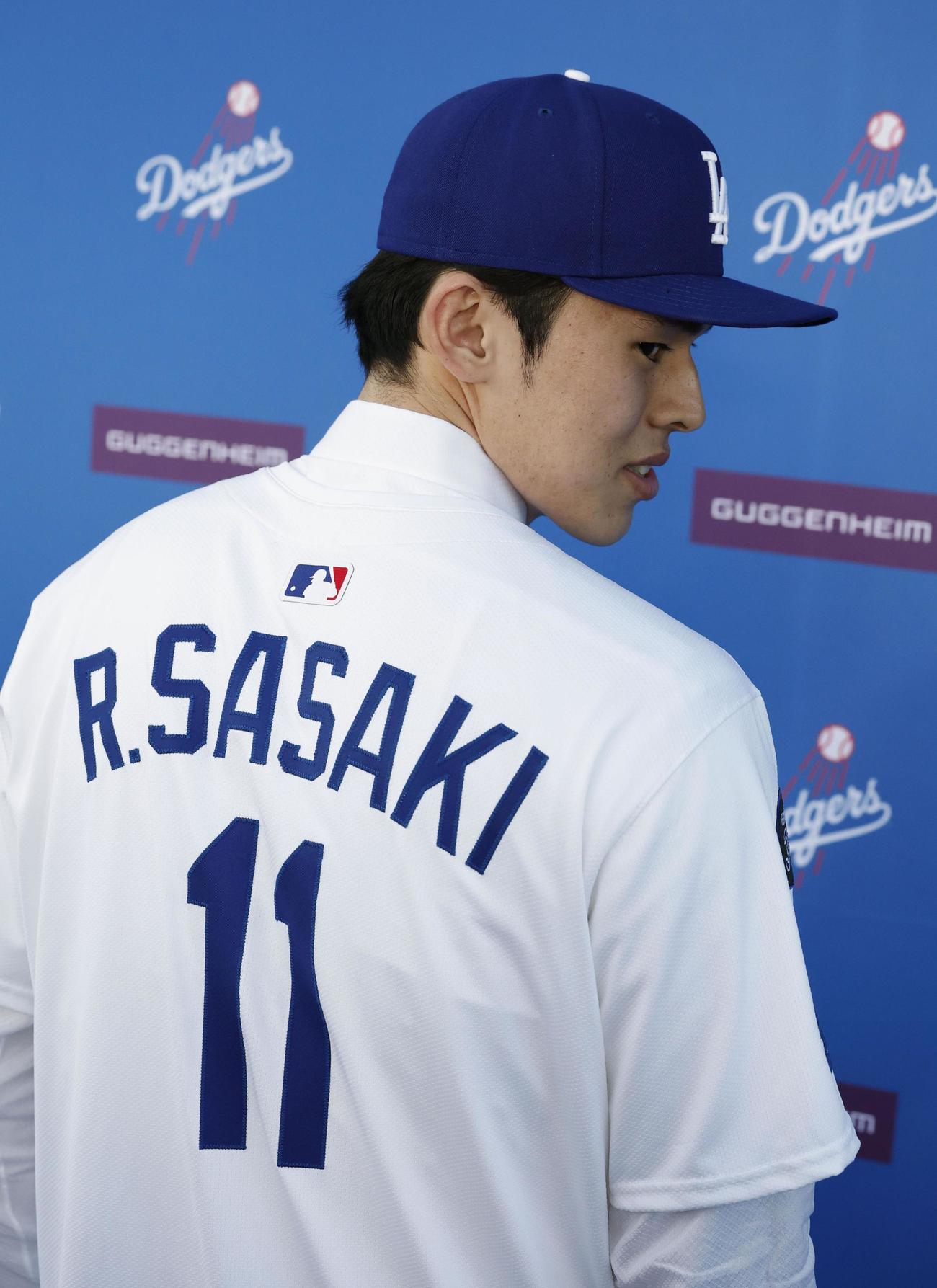 ドジャースの入団記者会見で背番号11のユニホームに袖を通し、撮影に応じる佐々木朗希投手。背ネームには「R.SASAKI」の文字が入った（共同）