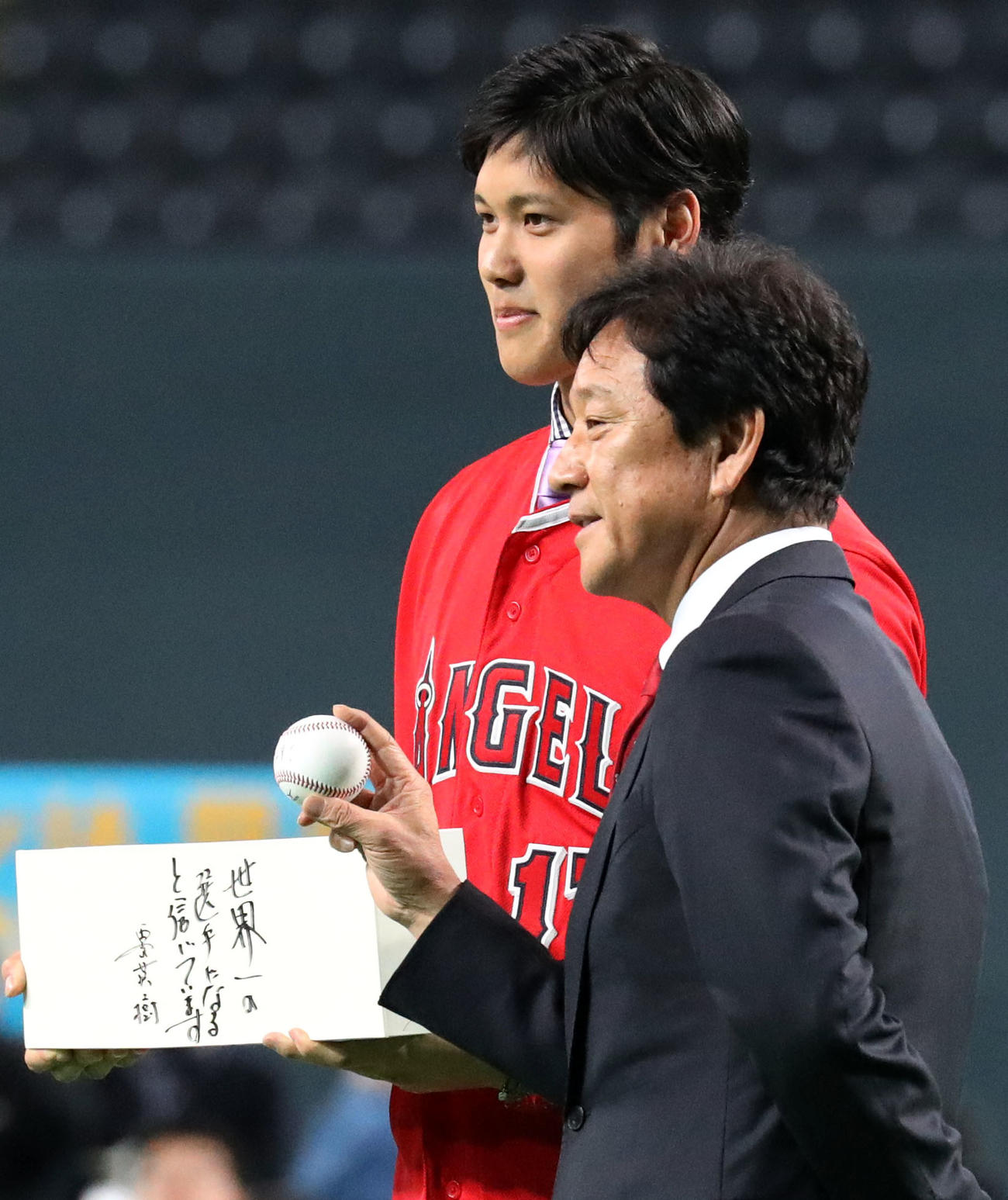 札幌ドームでの公開記者会見で「世界一の選手になると信じています」と書かれた記念品を栗山監督（手前）からもらう大谷（撮影・狩俣裕三）