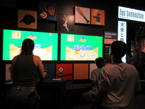 （9）日本の野球に関するポップカルチャーを紹介するコーナーで日本のテレビゲームに挑戦する米国の来館者