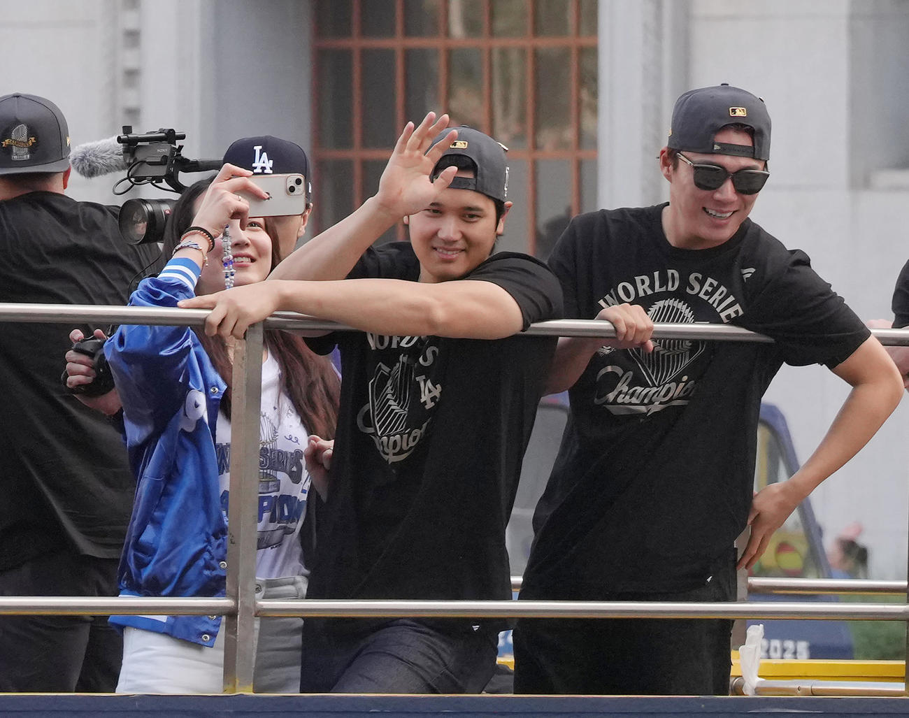 優勝パレードで沿道のファンに手を振るドジャース大谷と山本（右）。左は撮影する真美子夫人（撮影・菅敏）