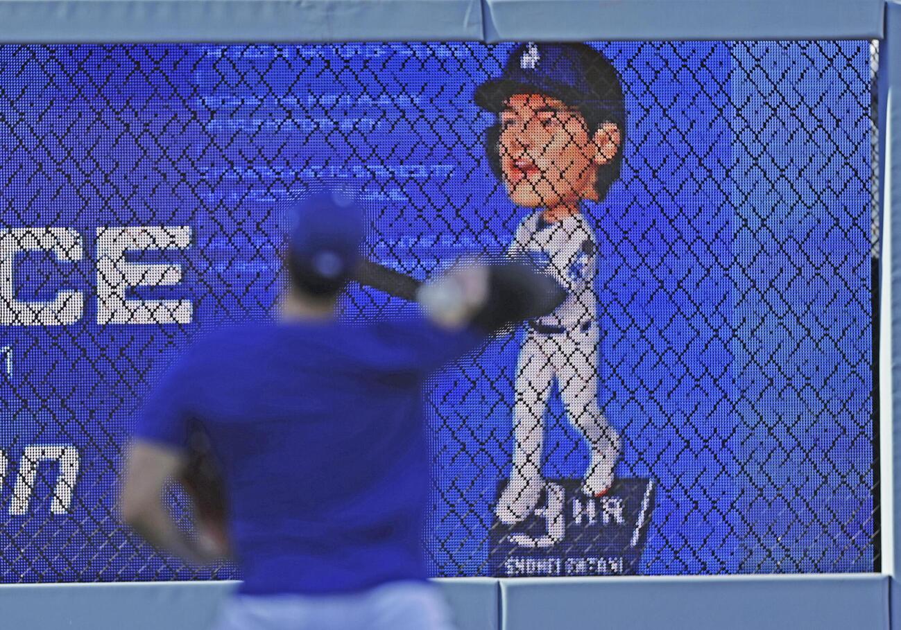 キャッチボールするドジャース大谷（手前）と、自身の首振り人形のモニター（共同）
