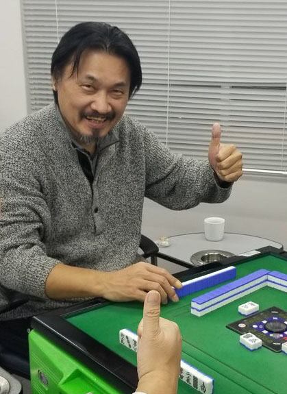 マージャン卓の前でサムアップポーズを決める加藤哲郎氏（同氏のツイッターより）