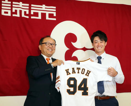 支配下登録会見で、球団旗を背に笑顔で背番号「94」のユニホームを手に記念撮影する加藤（右）と今村球団顧問（撮影・浅見桂子）