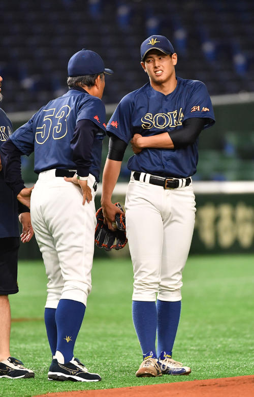 大工大対創価大　1回表創価大1死一塁、打者山本の時、一塁走者井上が二塁盗塁、その送球が背中に当たり痛がる杉山、左は岸監督（撮影・柴田隆二）