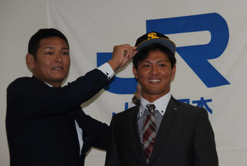 ソフトバンクのドラフト1位、JR西日本の佐藤（右）は、永井編成育成本部長兼スカウト育成部長に帽子をかぶせられて笑顔を見せる（撮影・浦田由紀夫）