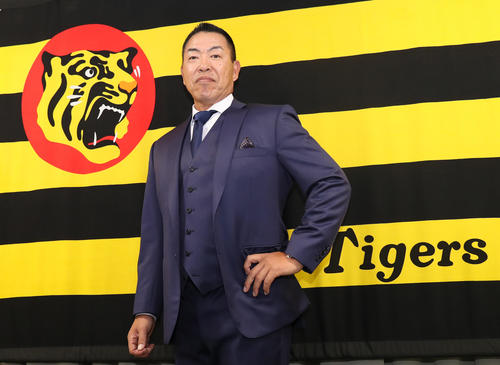 球団旗をバックにポーズを取る井上一樹新コーチ（撮影・白石智彦）