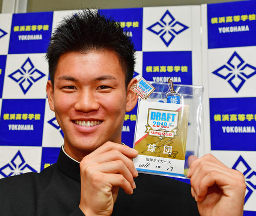 阪神の指名あいさつを受け矢野耀大監督のサイン入りドラフトIDを手に笑顔をみせるドラフト3位指名の横浜・及川雅貴（撮影・清水貴仁）