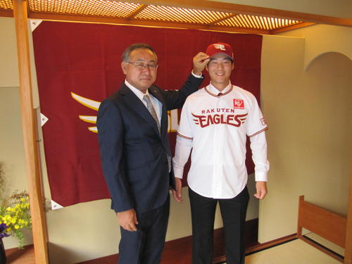 楽天から育成ドラフト3位で指名されたハワイ大・山崎（右）は入団合意し、後関スカウト部長から帽子とユニホームを渡され笑顔を見せる