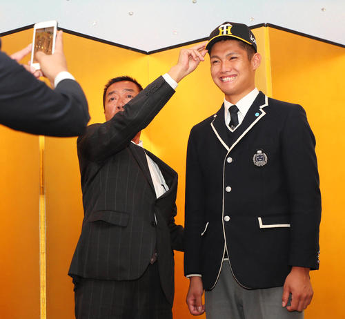 阪神と仮契約を結んだ創志学園・西純矢は、山本宣史担当スカウト（左）から帽子を被せてもらい、球団HPの撮影に臨む（撮影・宮崎幸一）
