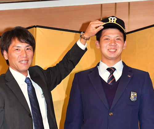 阪神との仮契約を終え、渡辺スカウト（左）に帽子をかぶせてもらい笑顔を見せる履正社・井上（撮影・上田博志）