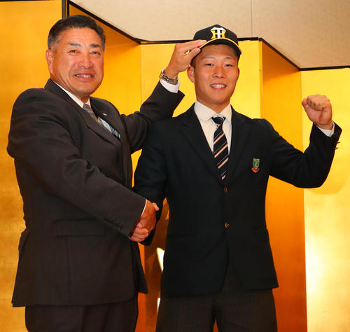 阪神と仮契約を結んだ藤田（右）は熊野担当スカウトに帽子をかぶせてもらい笑顔で握手を交わす（撮影・宮崎幸一）