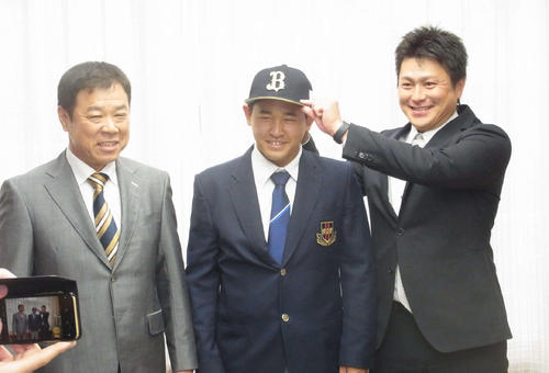 オリックスの1位指名あいさつを受け、縞田スカウト（右）から帽子をかぶせてもらう興南・宮城（中央）左は福良GM（2019年10月20日）