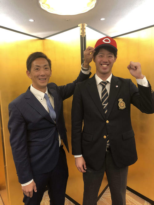 広島と仮契約を結び、尾形スカウト（左）から帽子をかぶせてもらい笑顔をみせるドラフト2位の法大・宇草（撮影・前原淳）