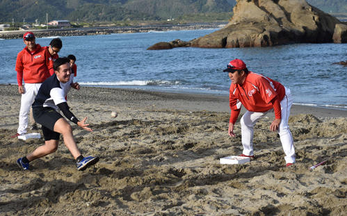 砂浜でチーム対抗リレーの罰ゲームとしてペッパートレーニングを行うケムナ（左）とボールをトスする佐々岡監督（右）