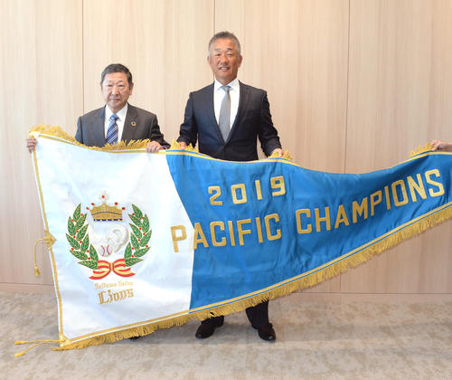 西武辻監督（右）は後藤オーナーとチャンピオンフラッグを掲げる（撮影・鈴木正章）