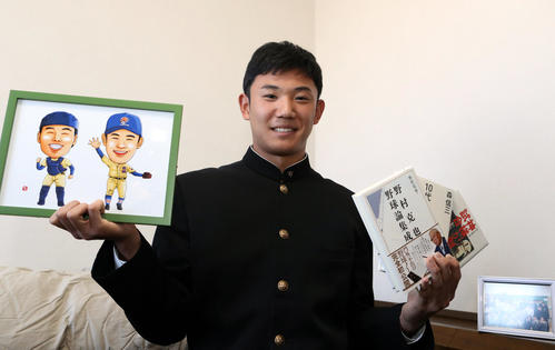 入寮し、星稜の山下名誉監督が持たせてくれた野村氏らの本と、山瀬とのバッテリーの似顔絵を手に笑顔を見せる奥川（撮影・狩俣裕三）