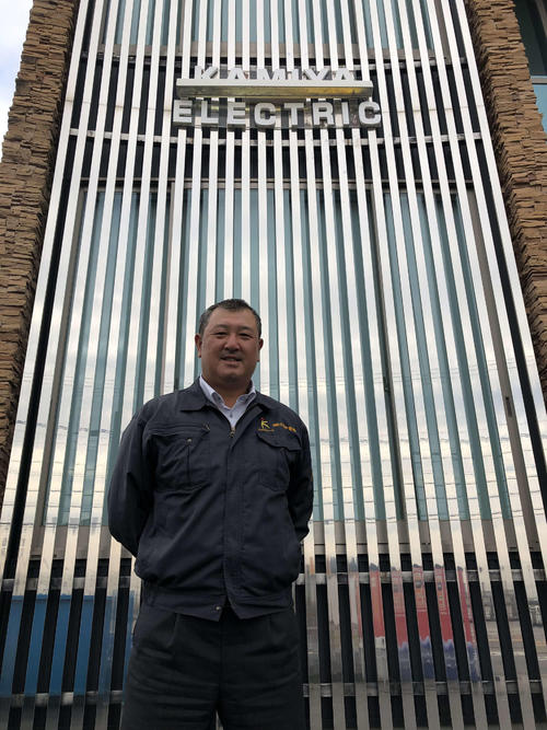 現在勤務するカミヤ電機本社前に立つ野口茂樹氏