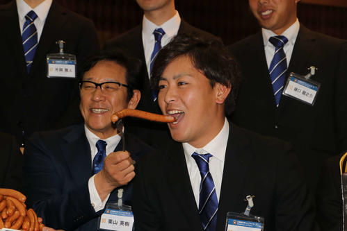 ニッポンハムグループの展示会に出席し栗山監督（左）から「シャウエッセン」を口に運ばれ笑顔で口を開く日本ハム河野（撮影・山崎純一）
