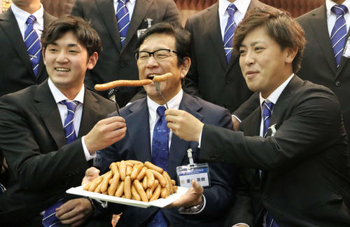 ニッポンハムグループの展示会に出席し、河野（右）と立野（左）から「シャウエッセン」を口に運ばれ笑顔で口を開く日本ハム栗山監督（撮影・山崎純一）