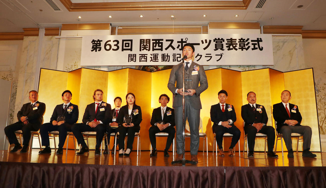 関西スポーツ賞の表彰式でスピーチする近本。後方は左から履正社の岡田監督、野口前主将、ファンデルヴァルト、古江、中村、山本由、関学大・鳥内監督、京産大・大西監督（撮影・加藤哉）