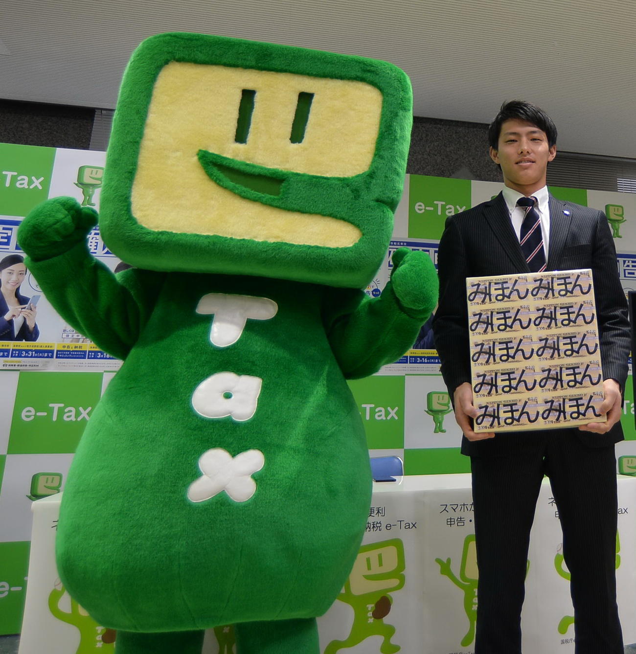 楽天辰己が国税庁キャラクターのイータ君と記念撮影。両手で1億円分のサンプル紙幣を持つ