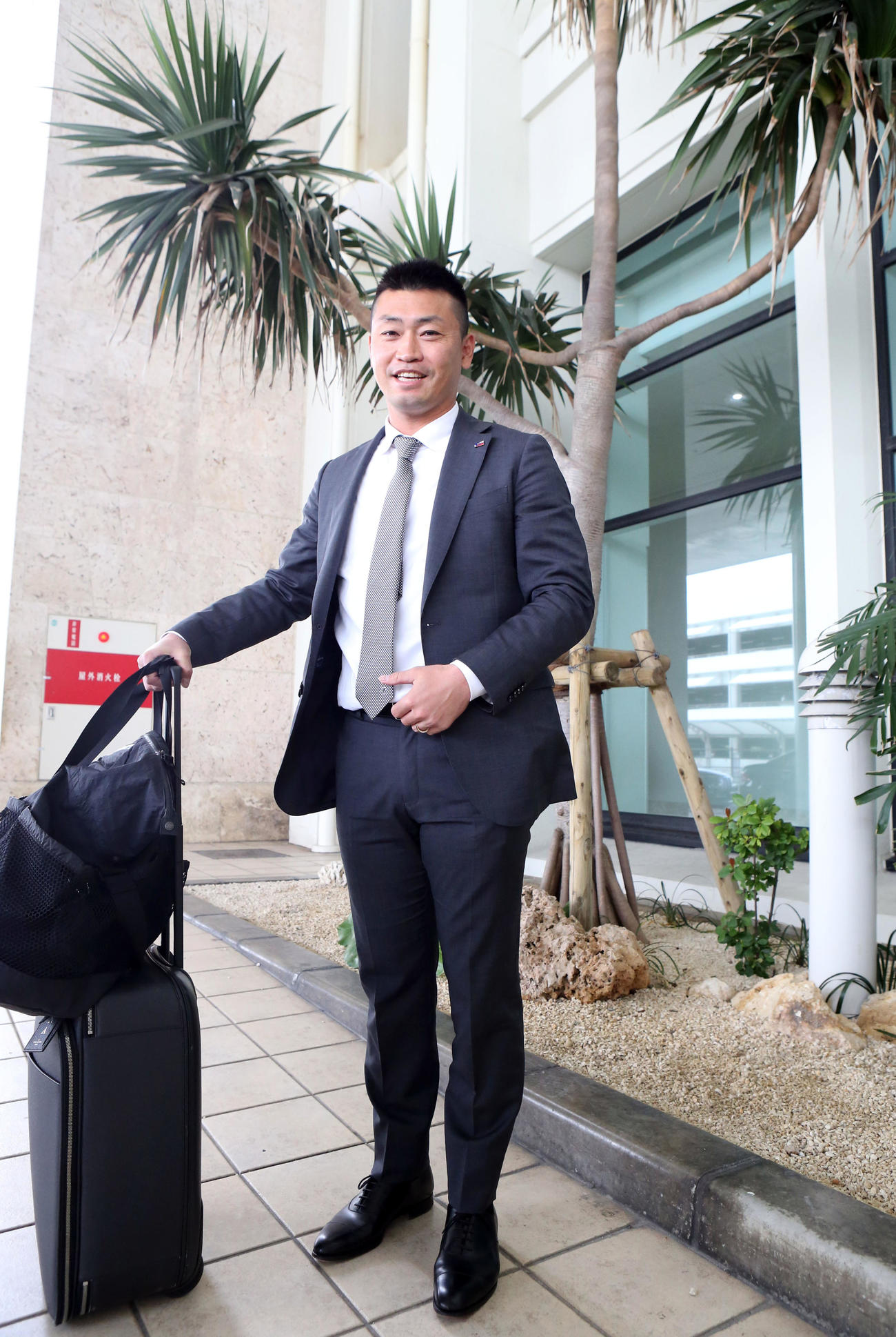 那覇空港に到着し、ヤシの木をバックに笑顔を見せる青木（撮影・狩俣裕三）