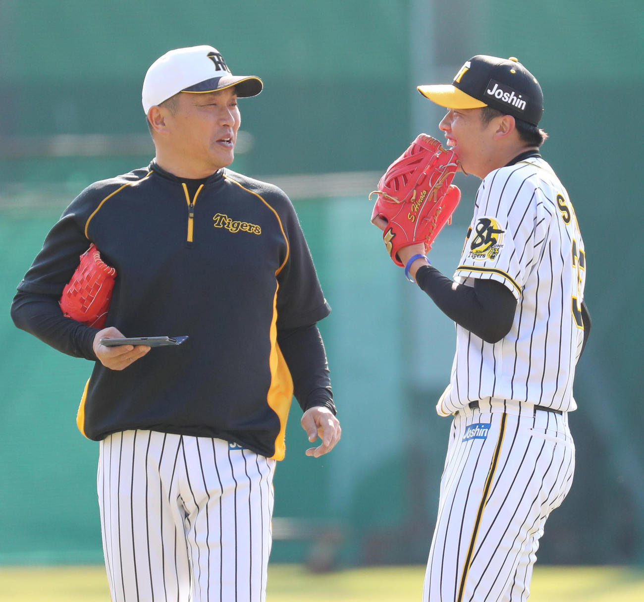 山本昌臨時投手コーチ（左）からスマートフォンの画面を見せられ笑顔となる才木（撮影・清水貴仁）