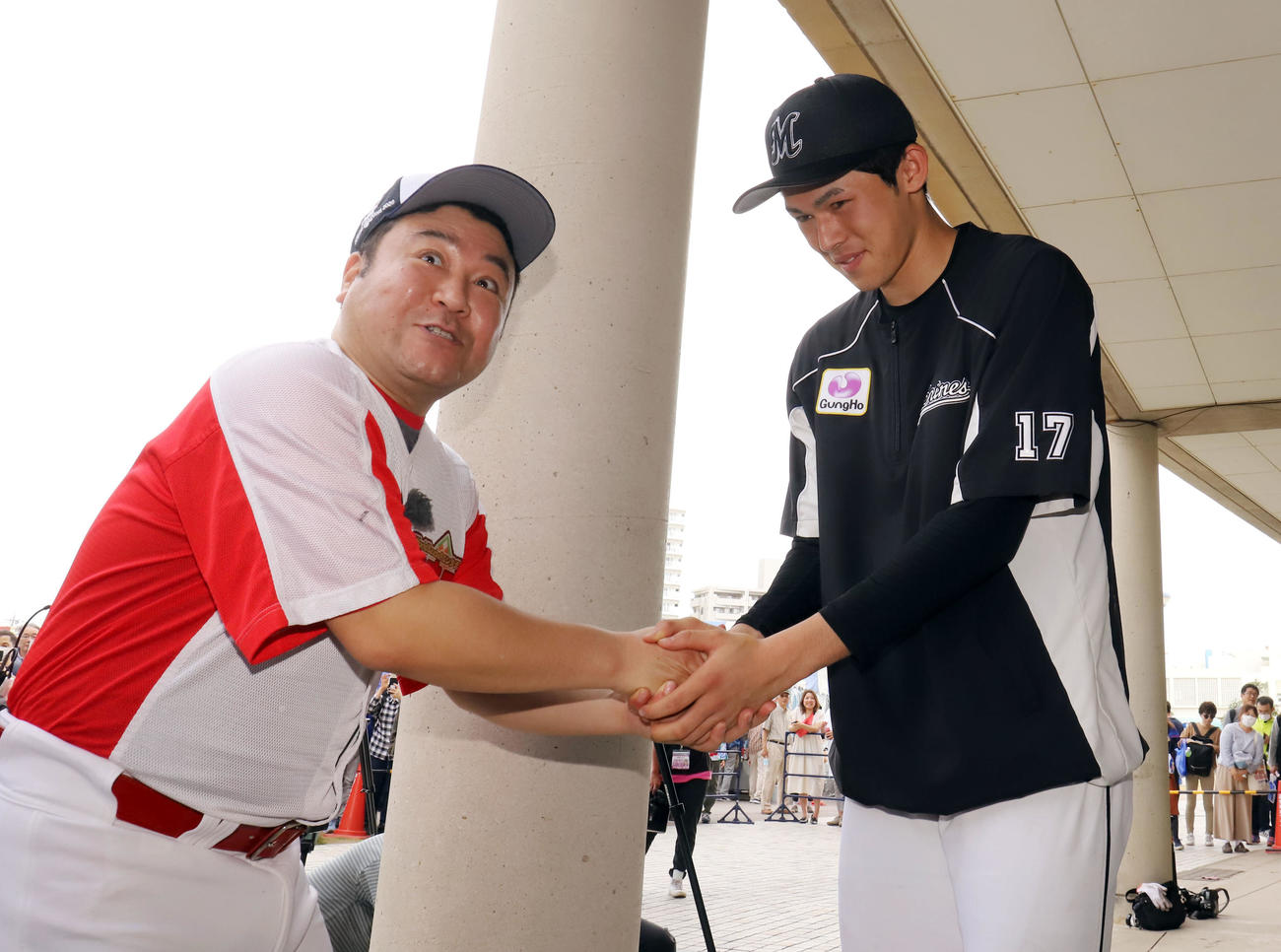 中日対ロッテ　テレビの取材できたアンタッチャブル山崎弘也（左）と握手を交わし笑顔を見せるロッテ佐々木朗（撮影・垰建太）