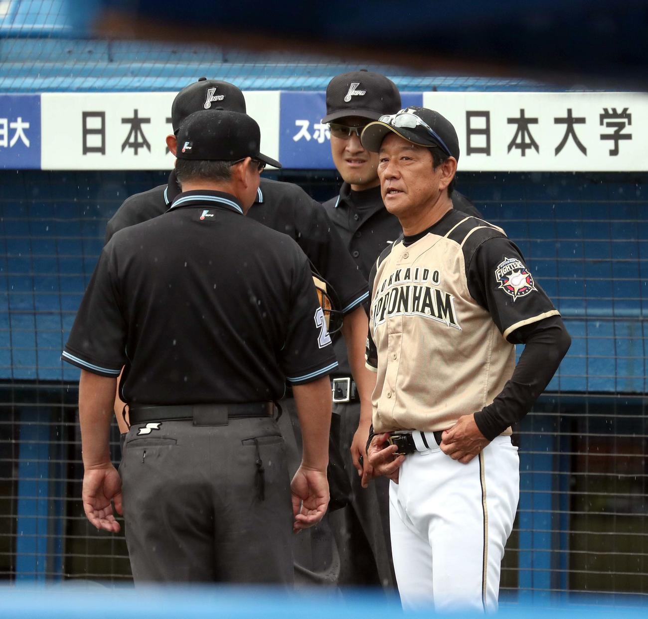 ヤクルト対日本ハム　雨が降る中、審判たちと会話する日本ハム栗山監督（撮影・佐藤翔太）
