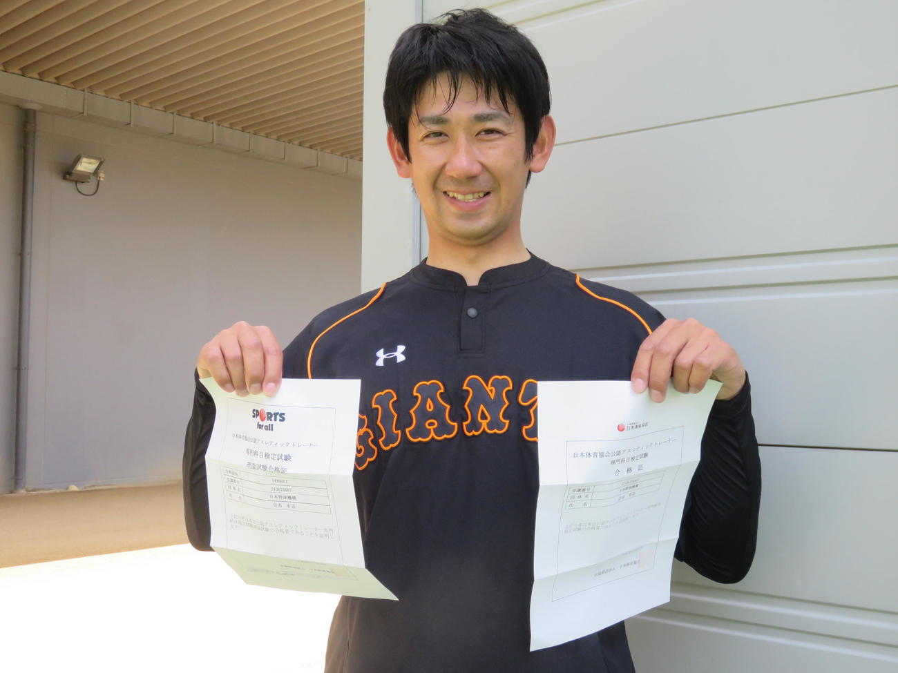 アスレティックトレーナー（AT）試験合格証を手に、笑顔の巨人会田コーチ（2016年4月18日撮影）