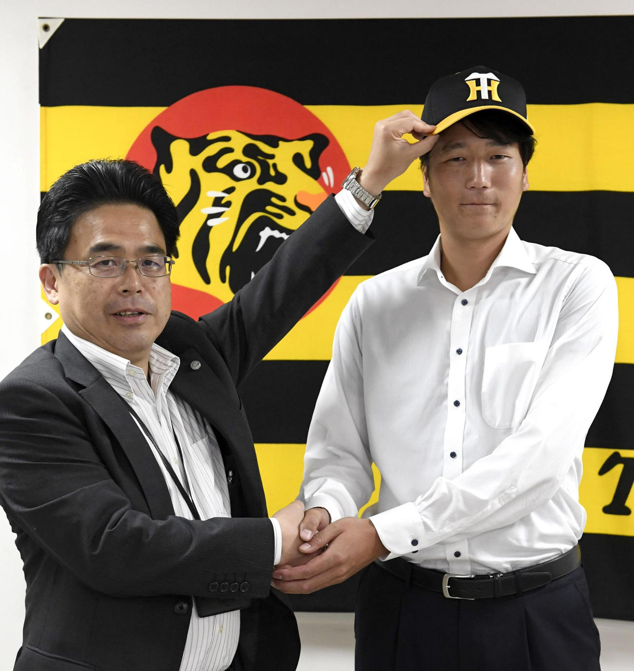 入団会見でポーズをとる小林慶祐。左は谷本球団本部長