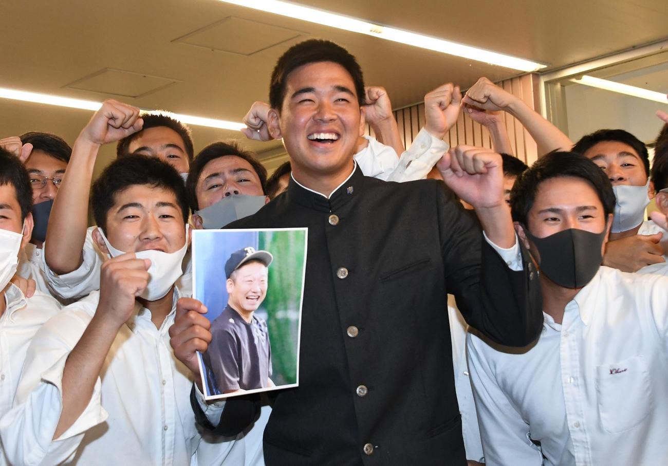 オリックスから1位指名を受けた福岡大大濠・山下は「新人王」と中嶋聡監督代行の写真を持って満面の笑みを浮かべる（撮影・今浪浩三）