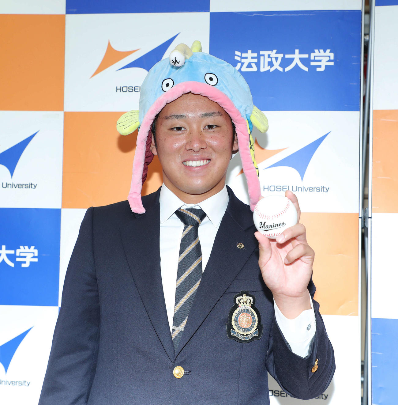 指名あいさつを終え、報道陣から渡された謎の魚の帽子をかぶり笑顔で写真に納まるロッテ１位指名の法大・鈴木（撮影・河田真司）