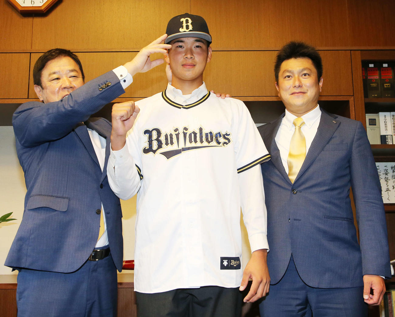 オリックスの指名あいさつを受け、福良GM（左）から帽子をかぶせてもらいガッツポーズするドラフト1位指名の福岡大大濠・山下（撮影・菊川光一）
