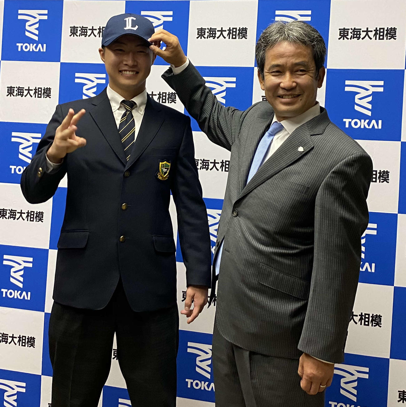 西武からドラフト3位指名を受けた東海大相模・山村は、西武潮崎球団本部編成グループディレクターから帽子をかぶせてもらい、目標の「3冠王」にあやかって指を3本立てる（撮影・湯本勝大）