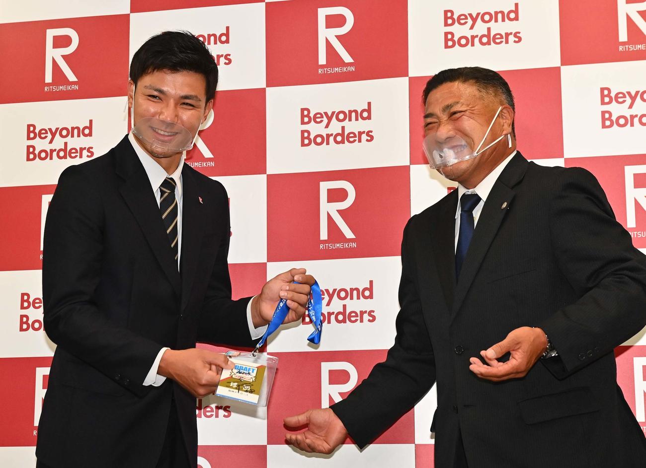 阪神熊光担当スカウト（右）から矢野監督サイン入りのドラフト会議入館証を手渡されるドラフト4位指名を受けた立命大・栄枝（撮影・上田博志）