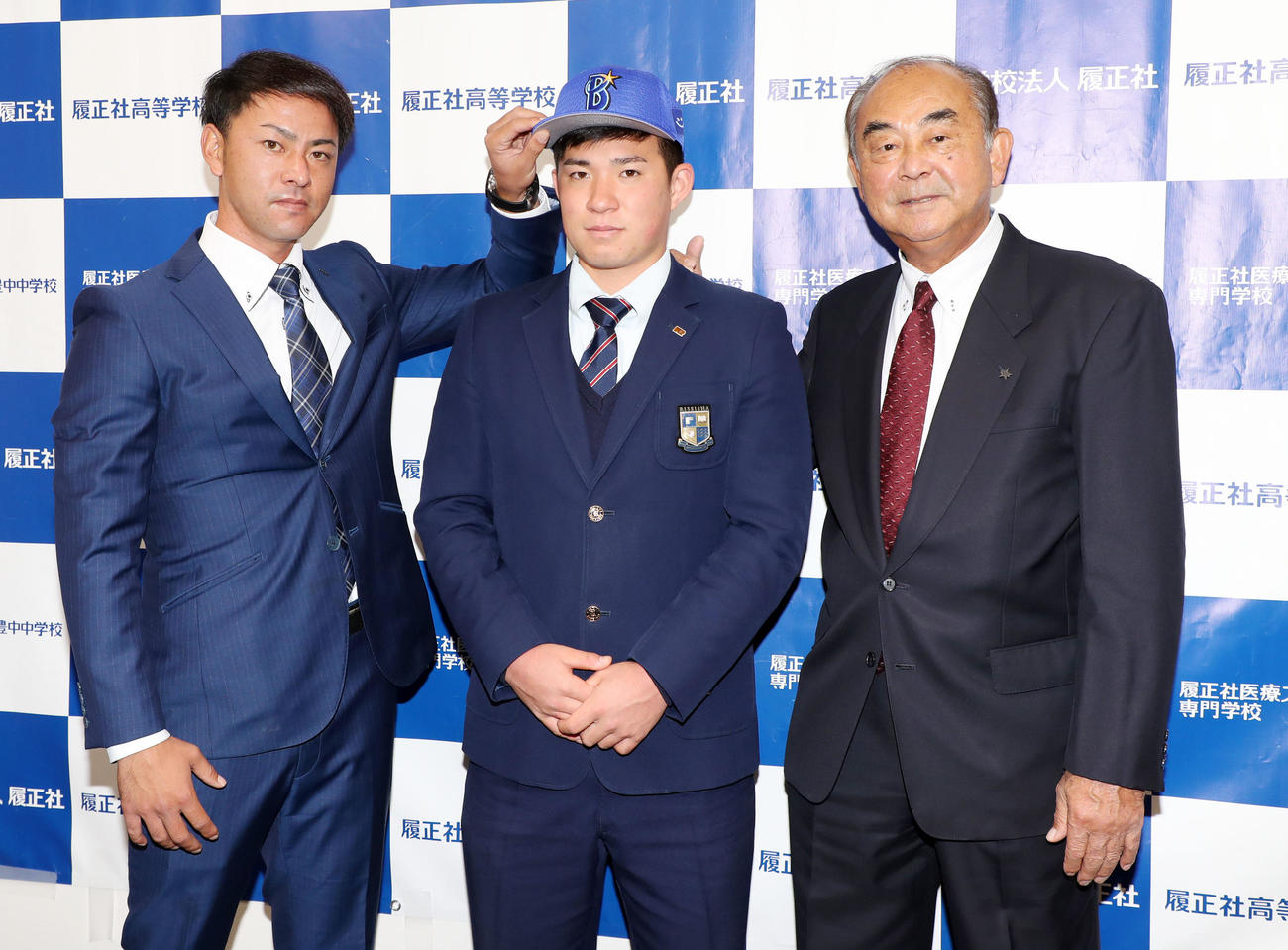 DeNAからドラフト指名あいさつを受け安部スカウト（左）から帽子をかぶせてもらう小深田、右は吉田顧問（撮影・加藤哉）