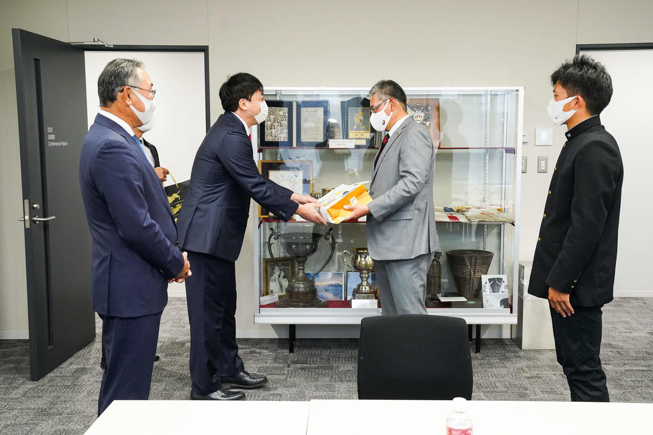 指名あいさつで仙台銘菓「萩の月」を早大・小宮山監督（中央右）へ手渡す楽天石井GM（中央左）。左は後関スカウト部長、右は早大・早川（球団提供）