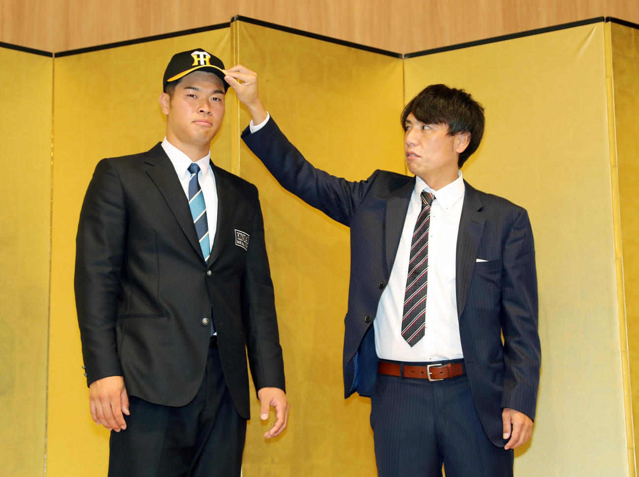 阪神との仮契約を終え、渡辺担当スカウト（右）に帽子をかぶせてもらう近大・佐藤輝明（撮影・前田充）
