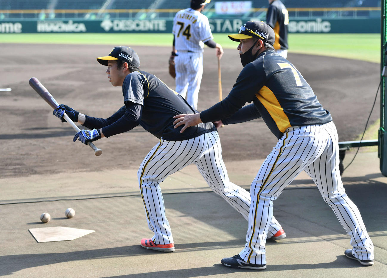 青柳晃洋（左）にバントの指導を行う久慈照嘉内野守備走塁コーチ（撮影・岩下翔太）