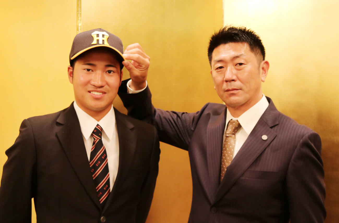 福岡市内のホテルで阪神と仮契約を結んだ岩田将（左）は田中スカウトから帽子をかぶせてもらう（阪神球団提供）