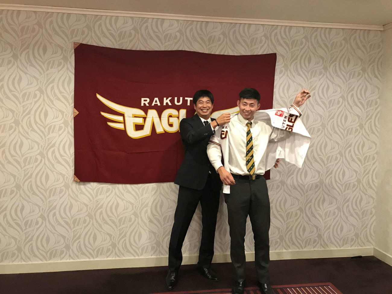 担当の宮越スカウト（左）からユニホームを着させてもらう楽天ドラフト5位の仙台育英・入江（右）（球団提供）