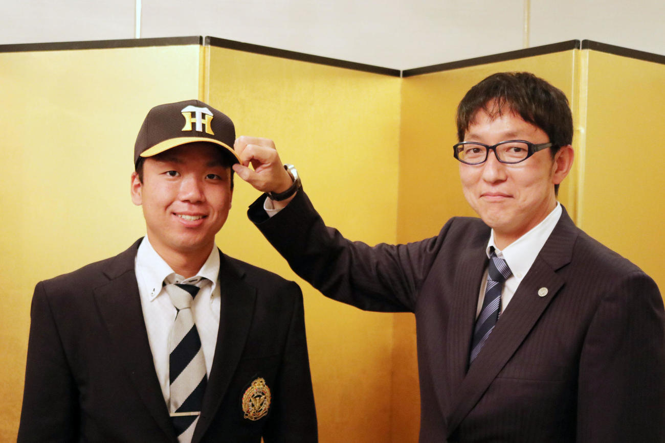 阪神と仮契約を結んだ村上（左）は吉野スカウトから帽子をかぶせてもらう（球団提供）