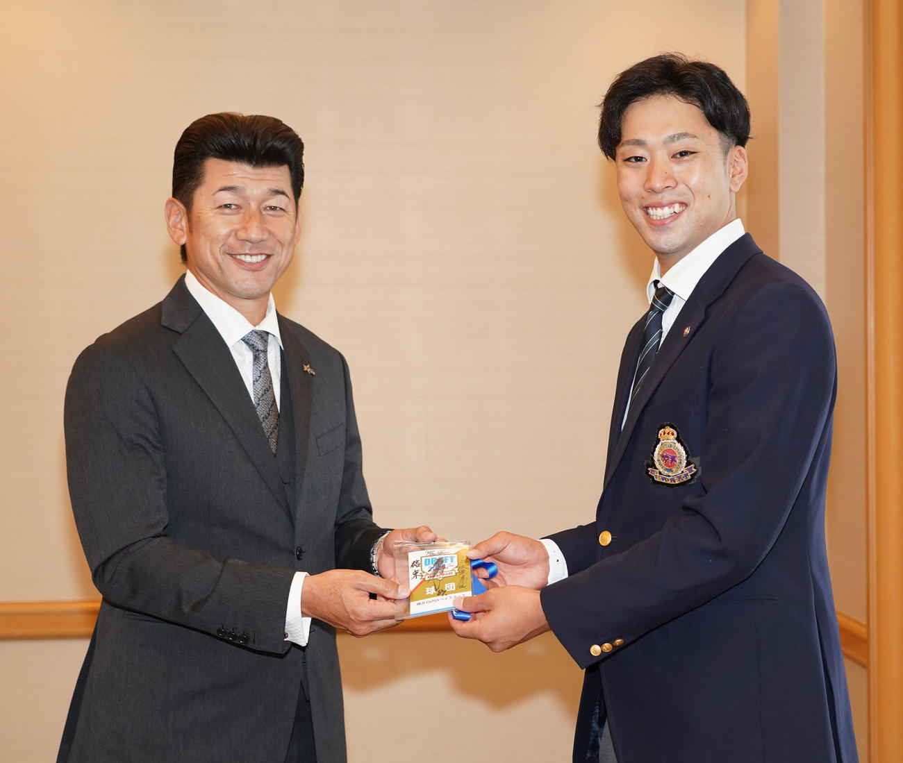 仮交渉で三浦大輔新監督（左）から「結束」と書かれたサイン入りドラフト会議入場証を受け取る明大・入江大生投手（代表撮影）