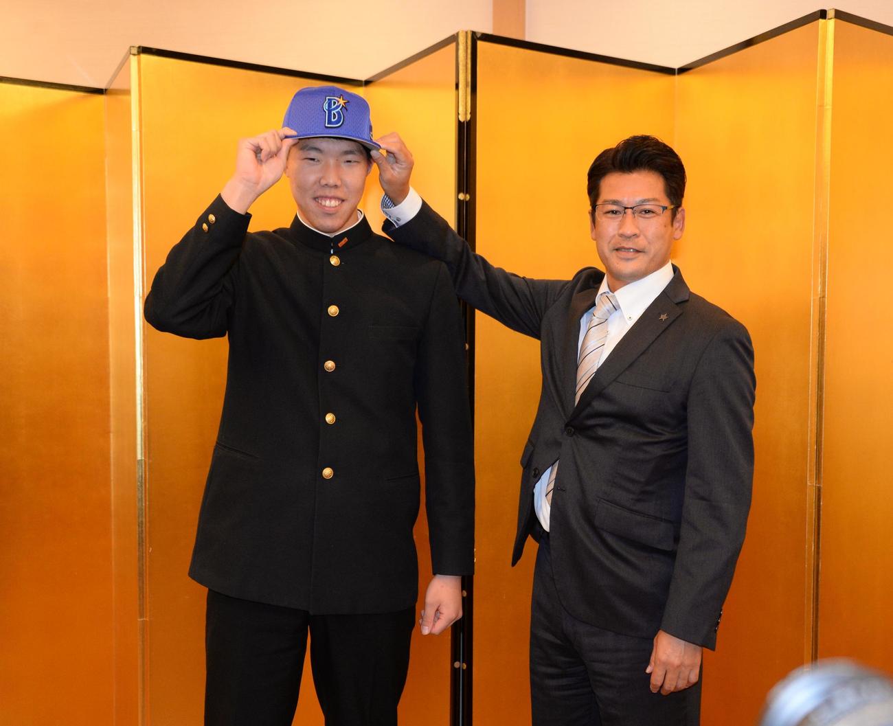 仮契約を終えたDeNAドラフト3位の横浜・松本（左）は稲嶺スカウトから帽子をかぶせてもらい笑顔を見せる（撮影・鈴木正章）