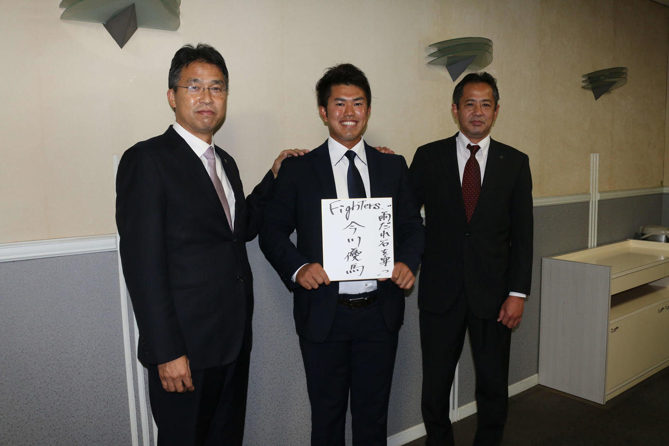 座右の銘「雨だれ石を穿つ」を書いた色紙を手にする今川（中央）は、日本ハム大渕スカウト部長（左）高橋スカウトに挟まれ笑顔（撮影・田中彩友美）