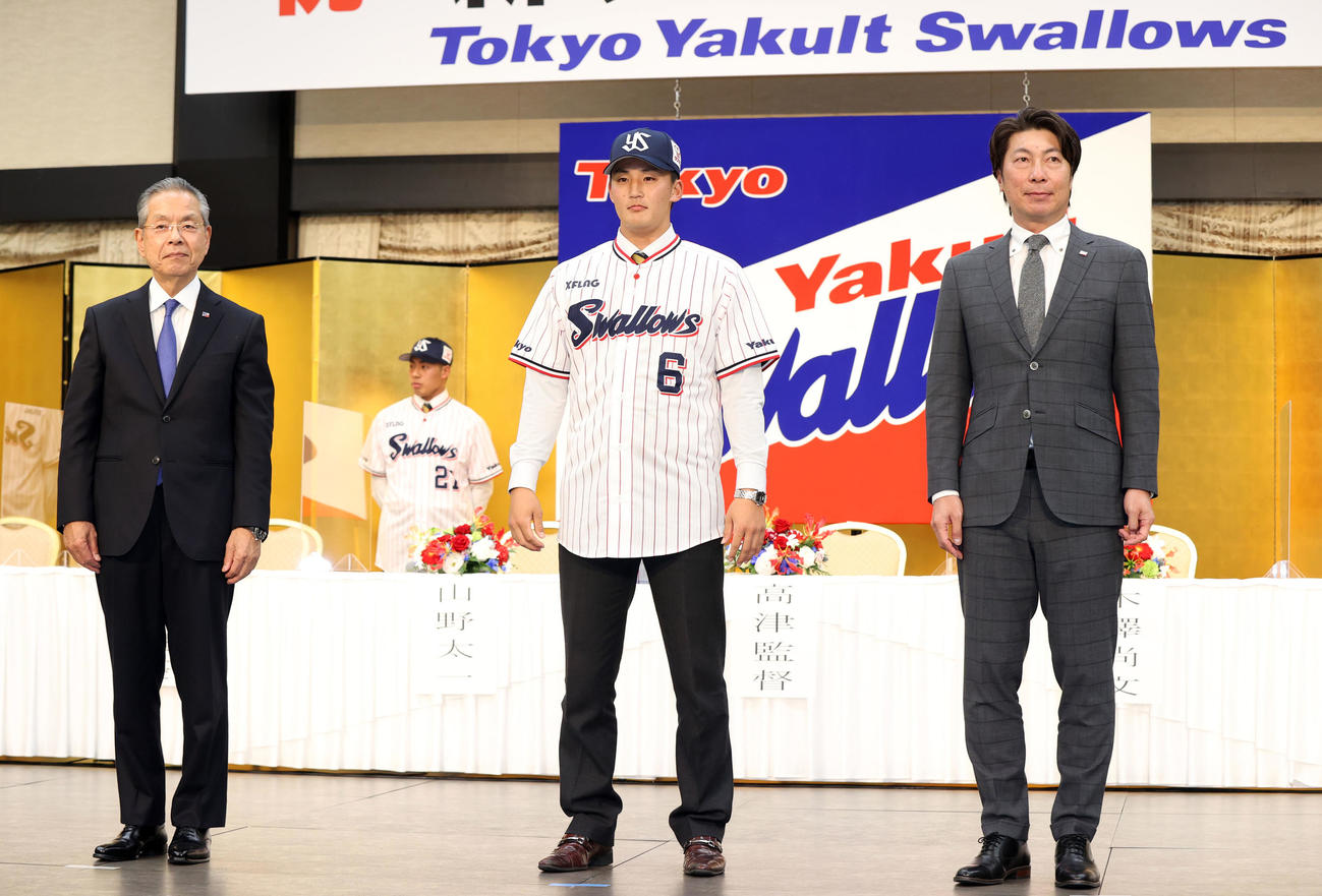 ヤクルト新入団発表会見で高津監督（右）からユニホームを着せてもらった後、記念撮影するドラフト4位の東北福祉大・元山（中央）。左は衣笠球団社長（撮影・狩俣裕三）