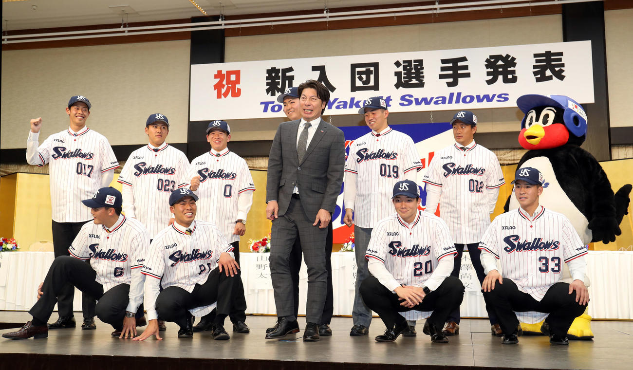 ヤクルト新入団発表会見で記念撮影で足がしびれて痛がる高津監督（前列中央）。前列左から4位東北福祉大・元山、2位東北福祉大・山野、1人おいて1位慶大・木沢、3位星稜・内山、後列左から育成4位丸山、育成2位BC信濃・赤羽、3位獨協大・並木、6位日本航空石川・嘉手苅、育成1位健大高崎・下、育成3位BC信濃・松井、つば九郎（撮影・狩俣裕三）