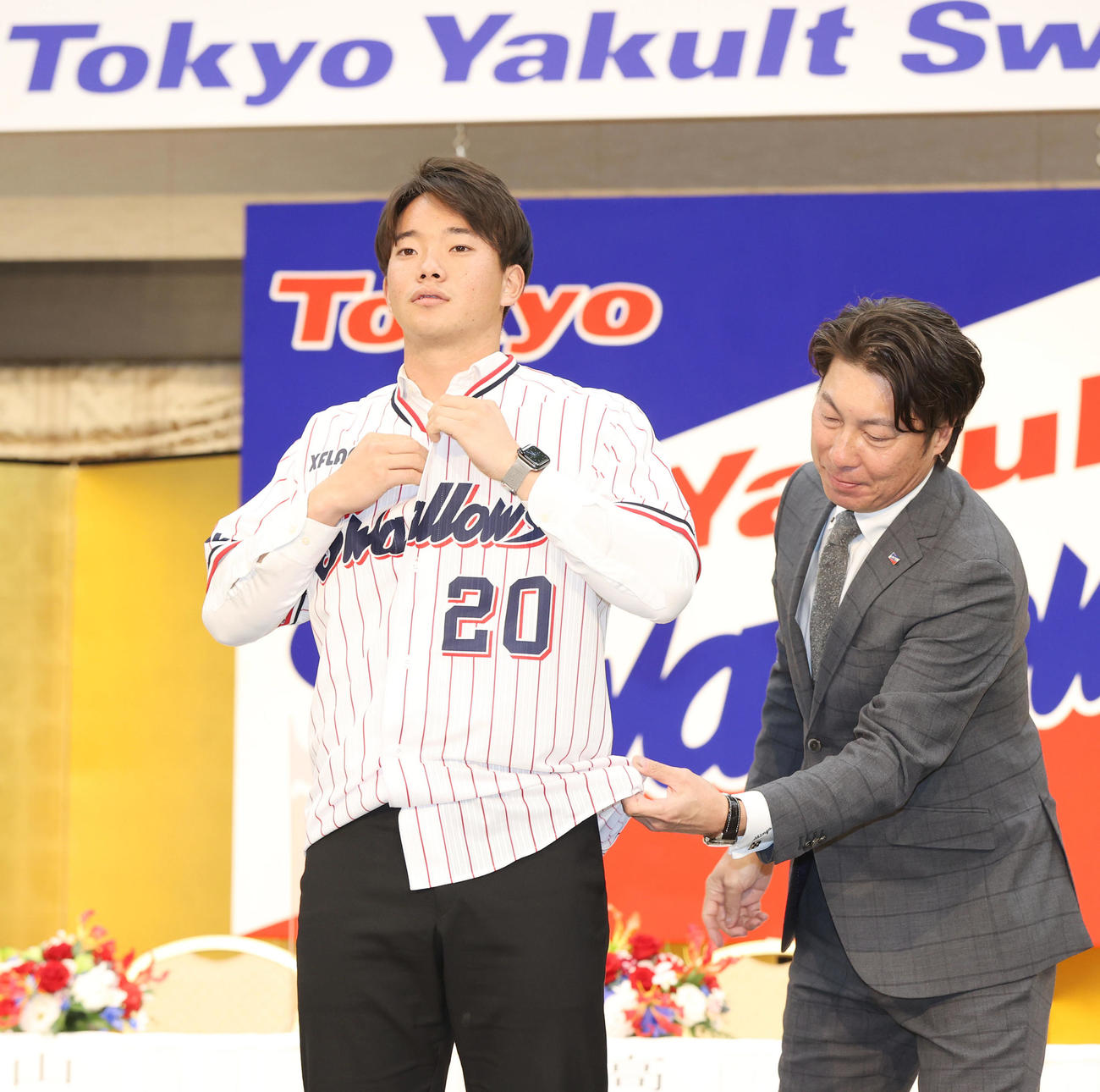 ヤクルト新入団発表会見で高津監督（右）からユニホームを着せてもらうドラフト1位の慶大・木沢（撮影・狩俣裕三）
