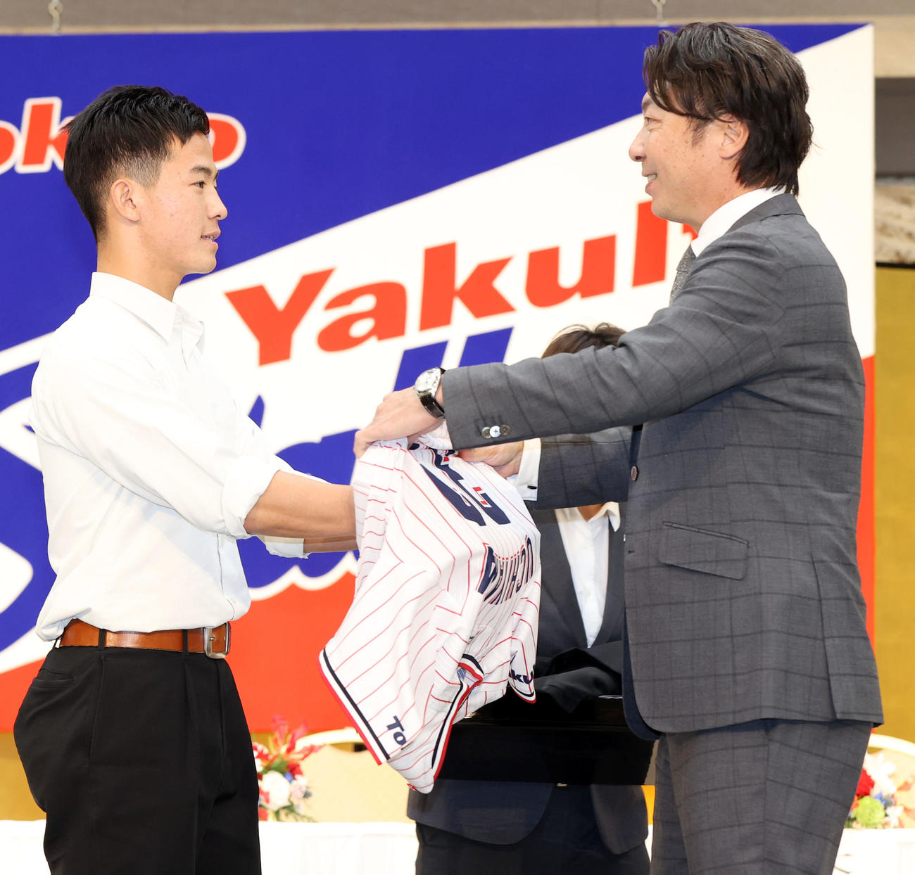 ヤクルト新入団発表会見で高津監督（右）からユニホームを着せてもらうドラフト3位の星稜・内山（撮影・狩俣裕三）